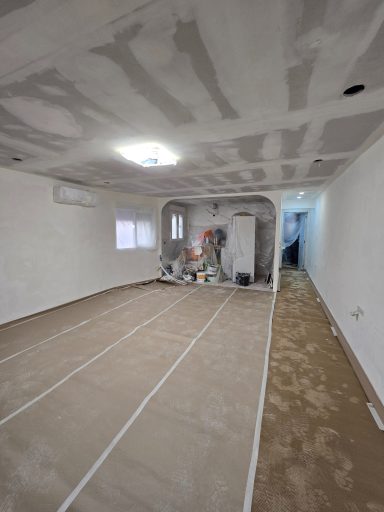 Sala en renovación con paredes sin pintar, suelo cubierto y herramientas de construcción.